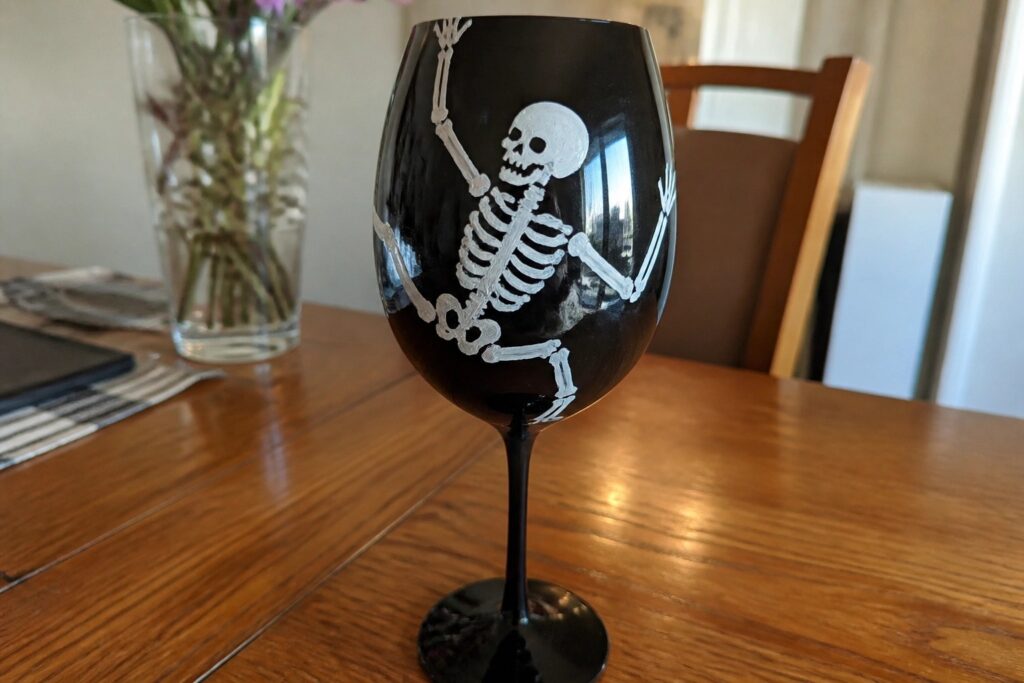 Clear wine glass etched with waving white skeleton on wooden table