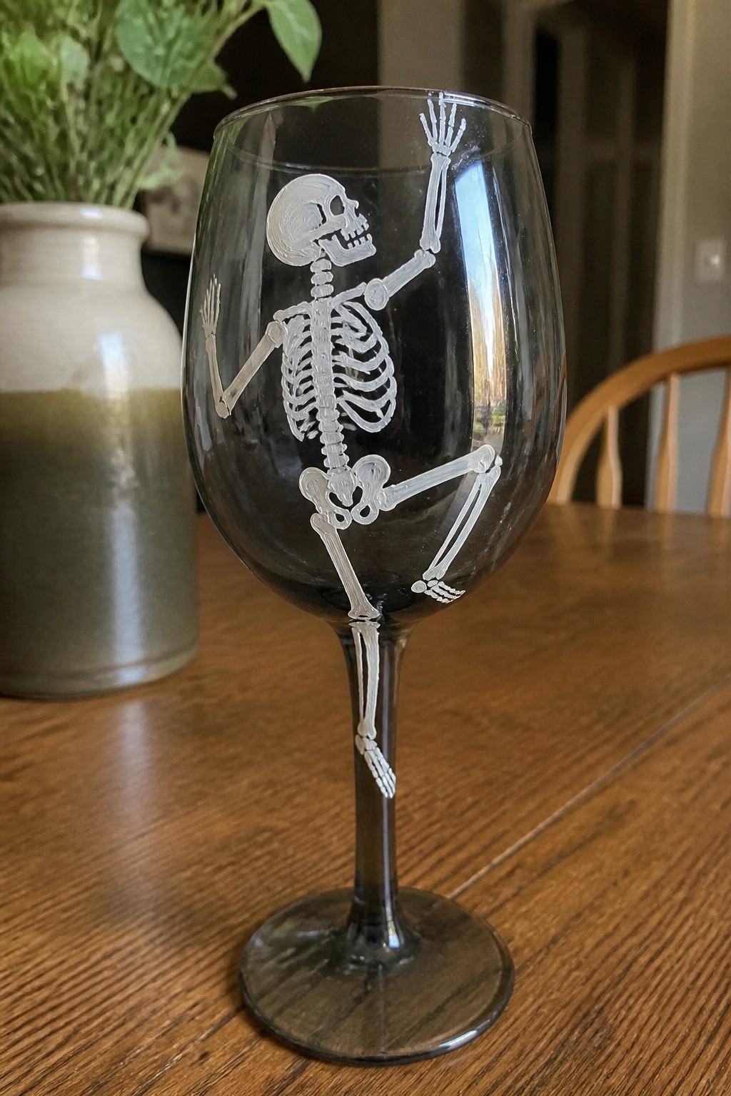Clear wine glass etched with waving white skeleton on wooden table