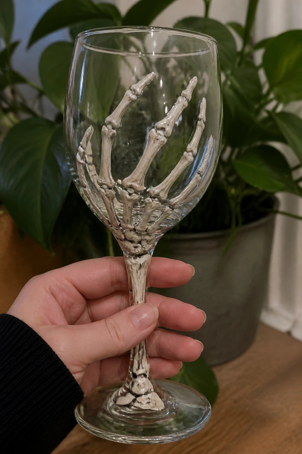 Hand holding clear wine glass with white skeleton hand and bone stem design.