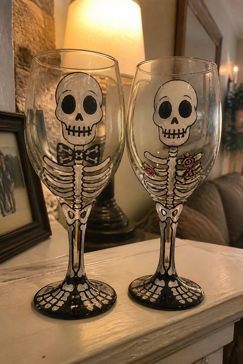 Two wine glasses painted with skeletons, one with bow tie and one with roses.