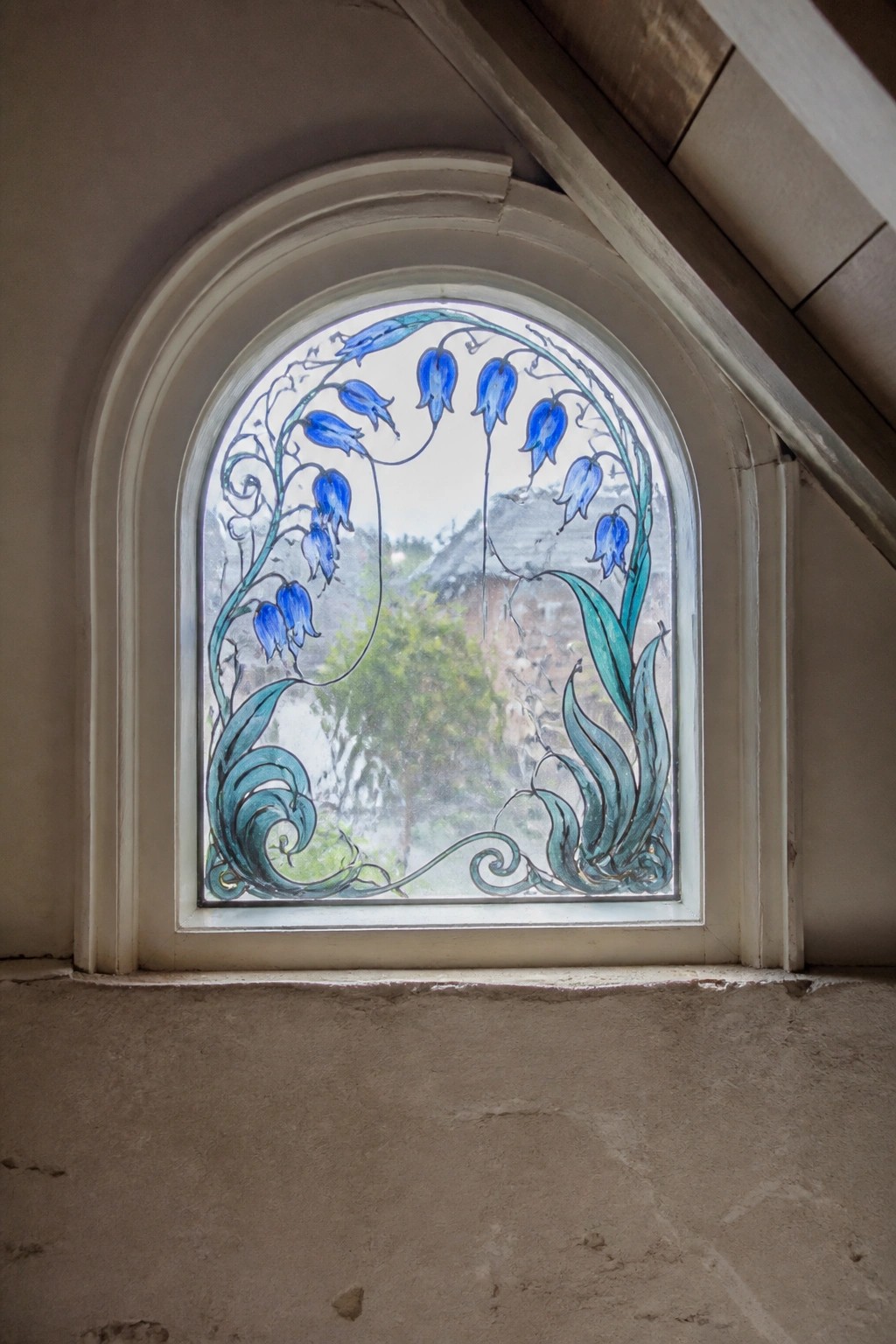 Arched window with stained glass showing blue bell flowers and teal leaves on a vine.