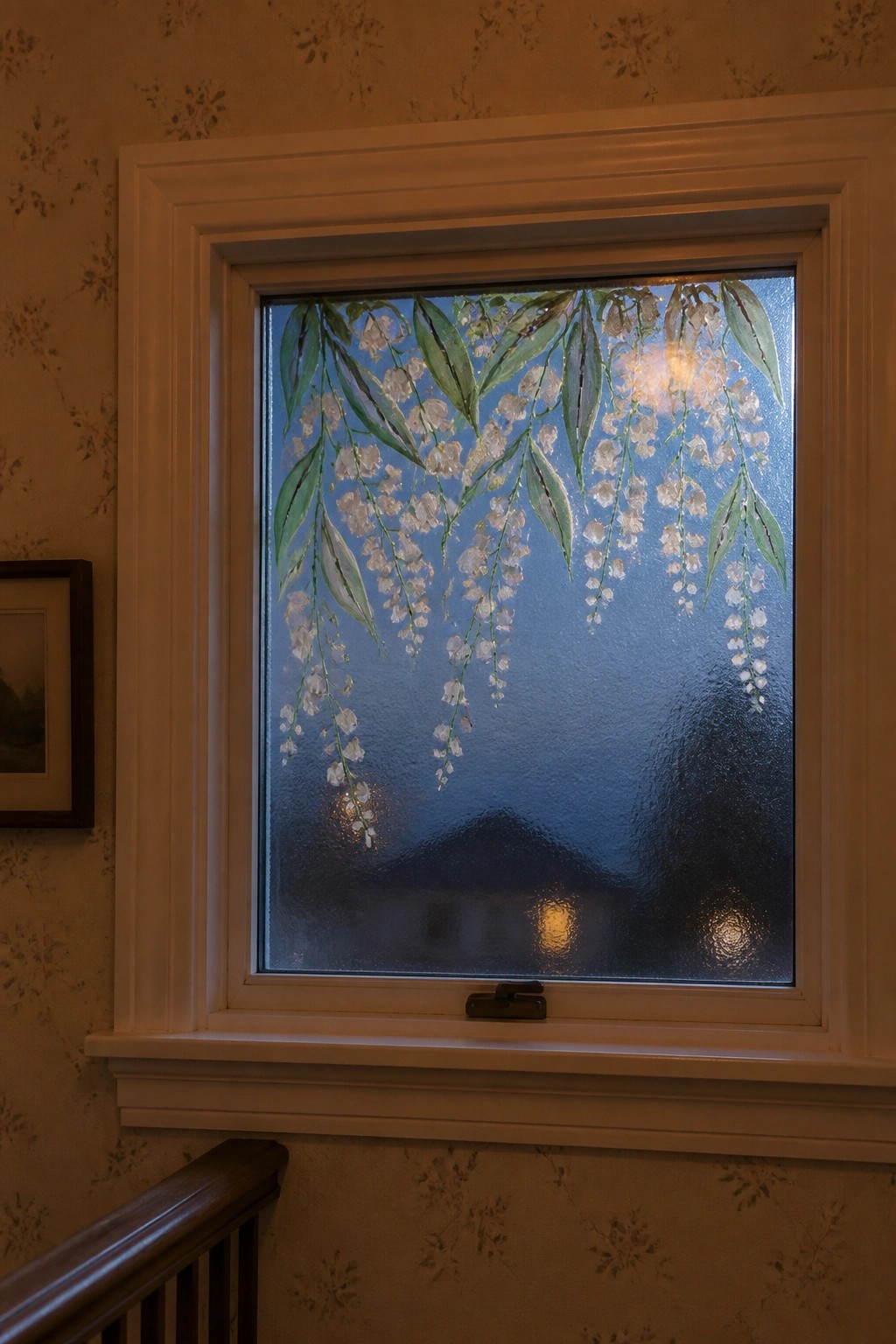 White-framed window with painted white flowers and green leaves on textured glass.