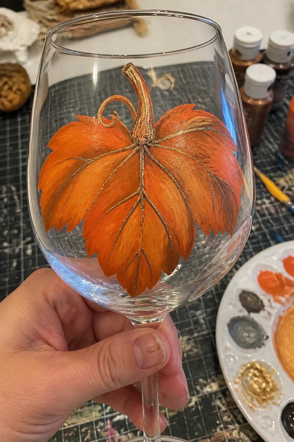 Hand holding wine glass with orange leaf and gold glitter stem painting.