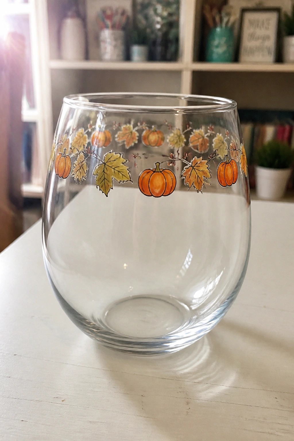 Clear stemless wine glass with orange pumpkins and autumn leaves on white table