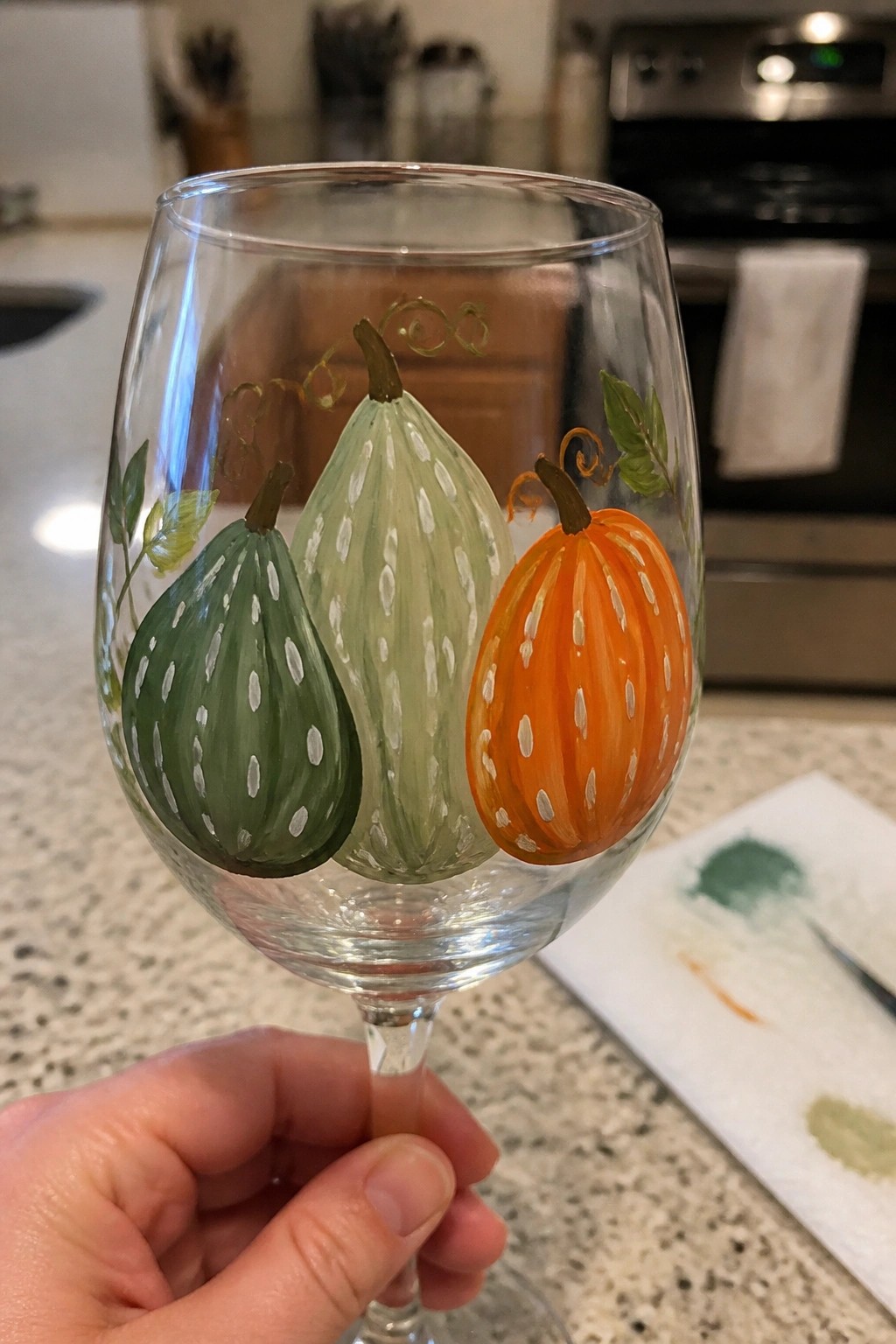 Hand holding wine glass painted with green and orange pumpkins and vines