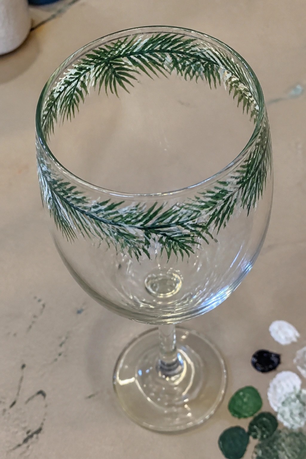 Clear wine glass with green pine branches and white accents painted on rim