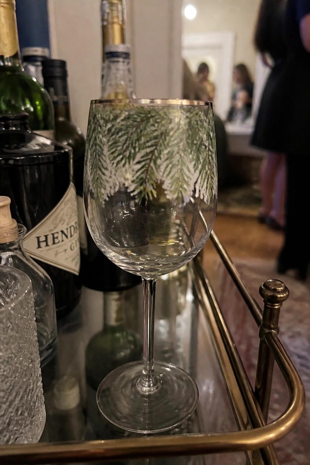 Wine glass with green pine design on brass bar cart amid liquor bottles