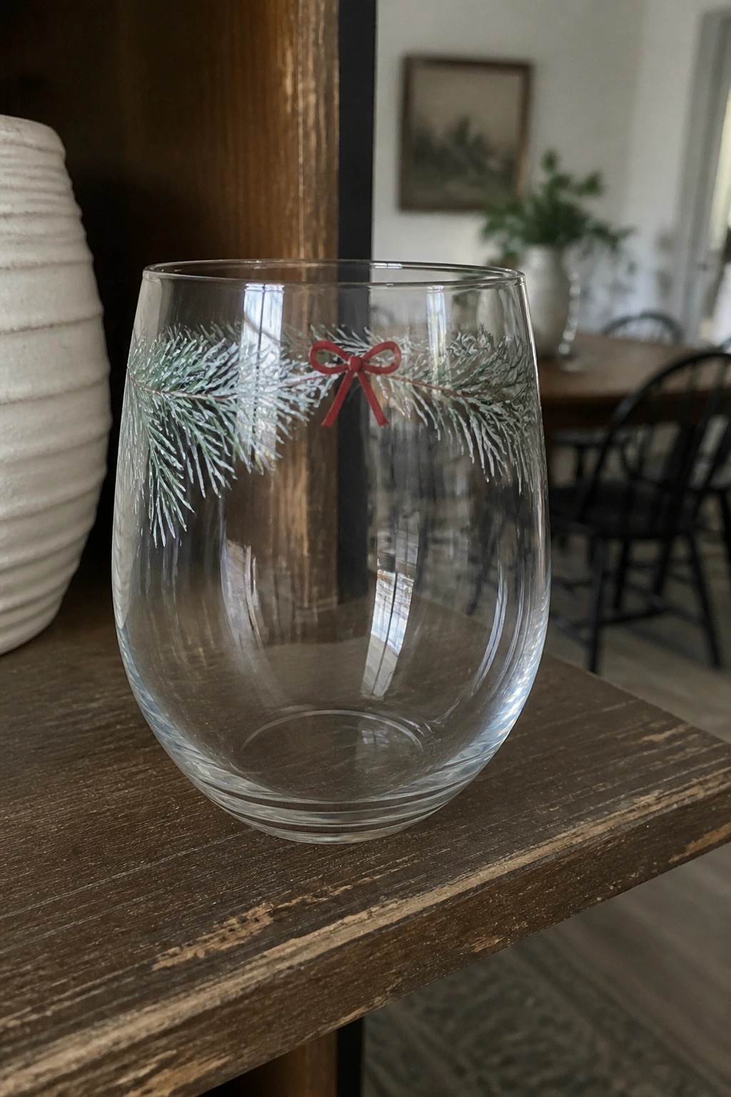 Clear stemless glass with green pine branches and red bow on wooden table.
