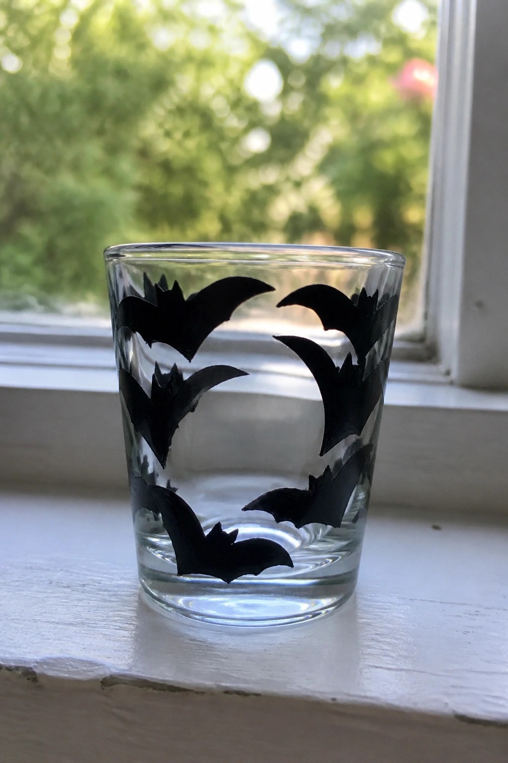 Clear glass tumbler with black bat silhouettes on white windowsill