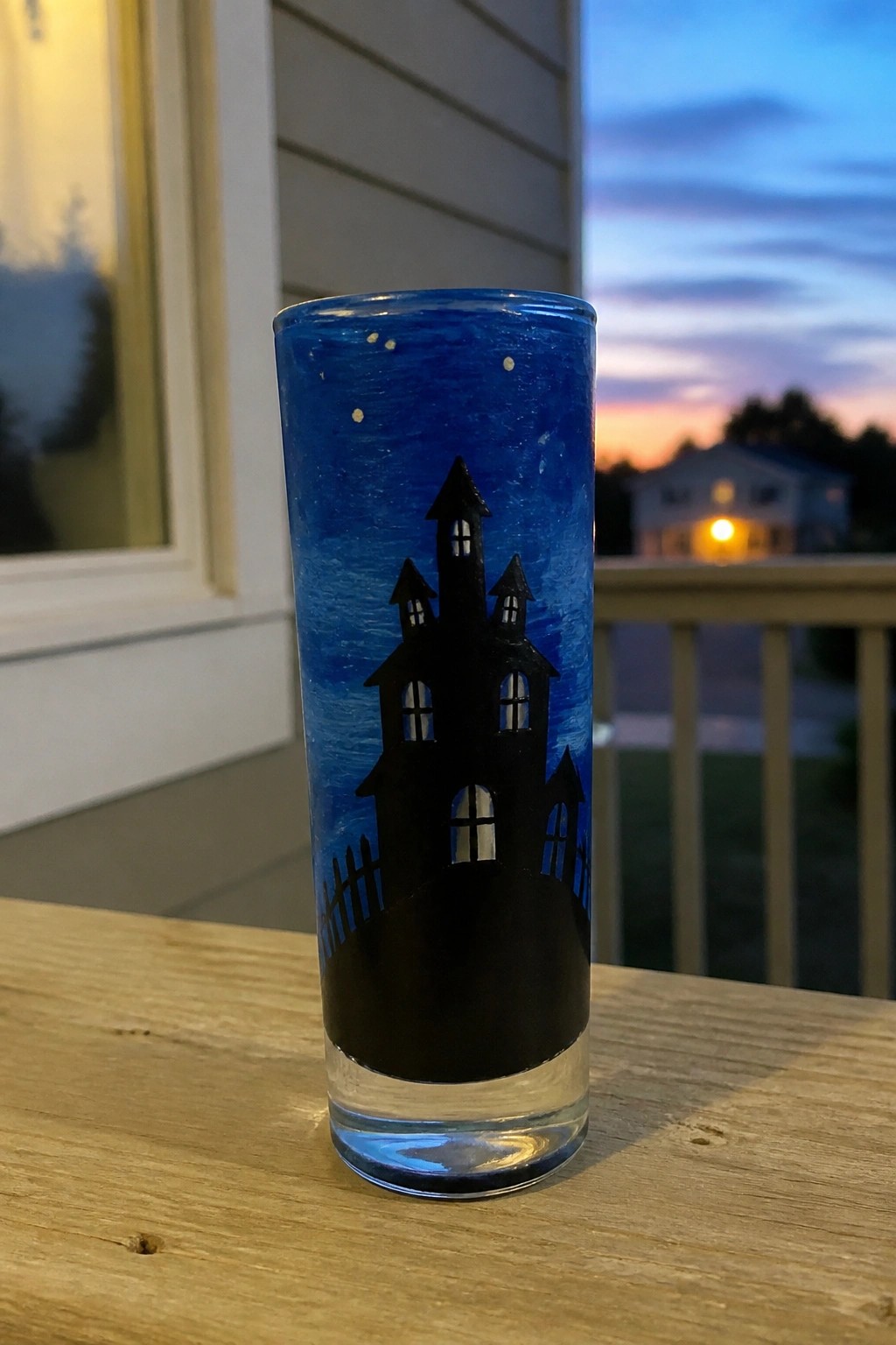Painted glass with black haunted house and fence on starry blue night background.