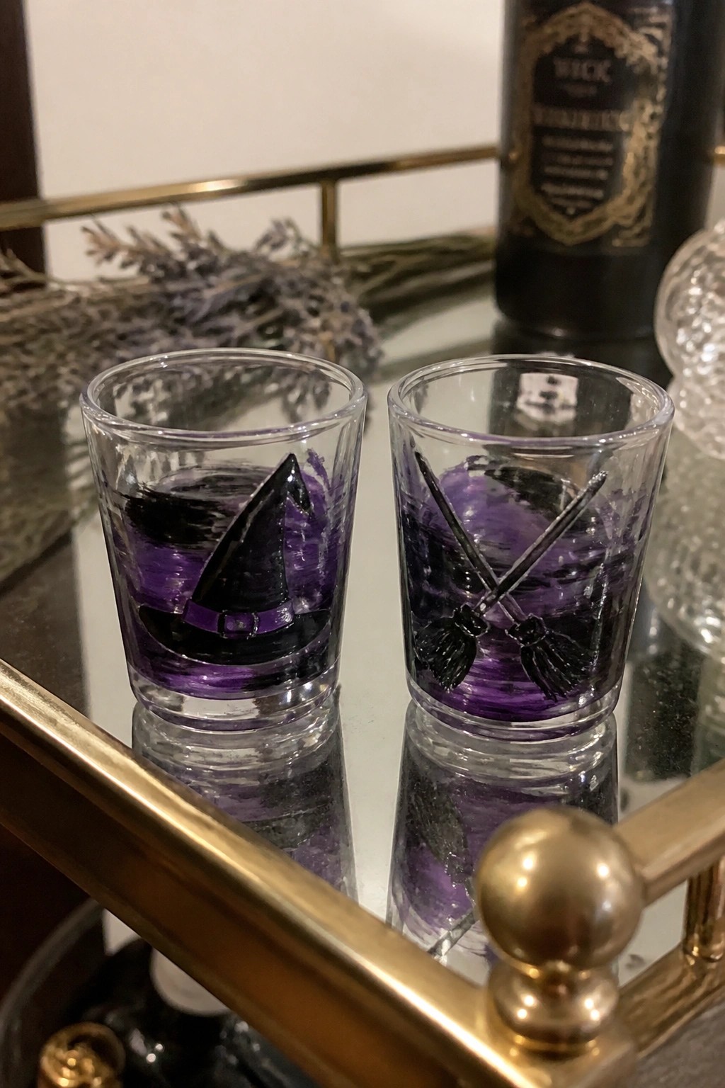 Two purple-painted shot glasses with witch hat and crossed brooms on gold mirror tray