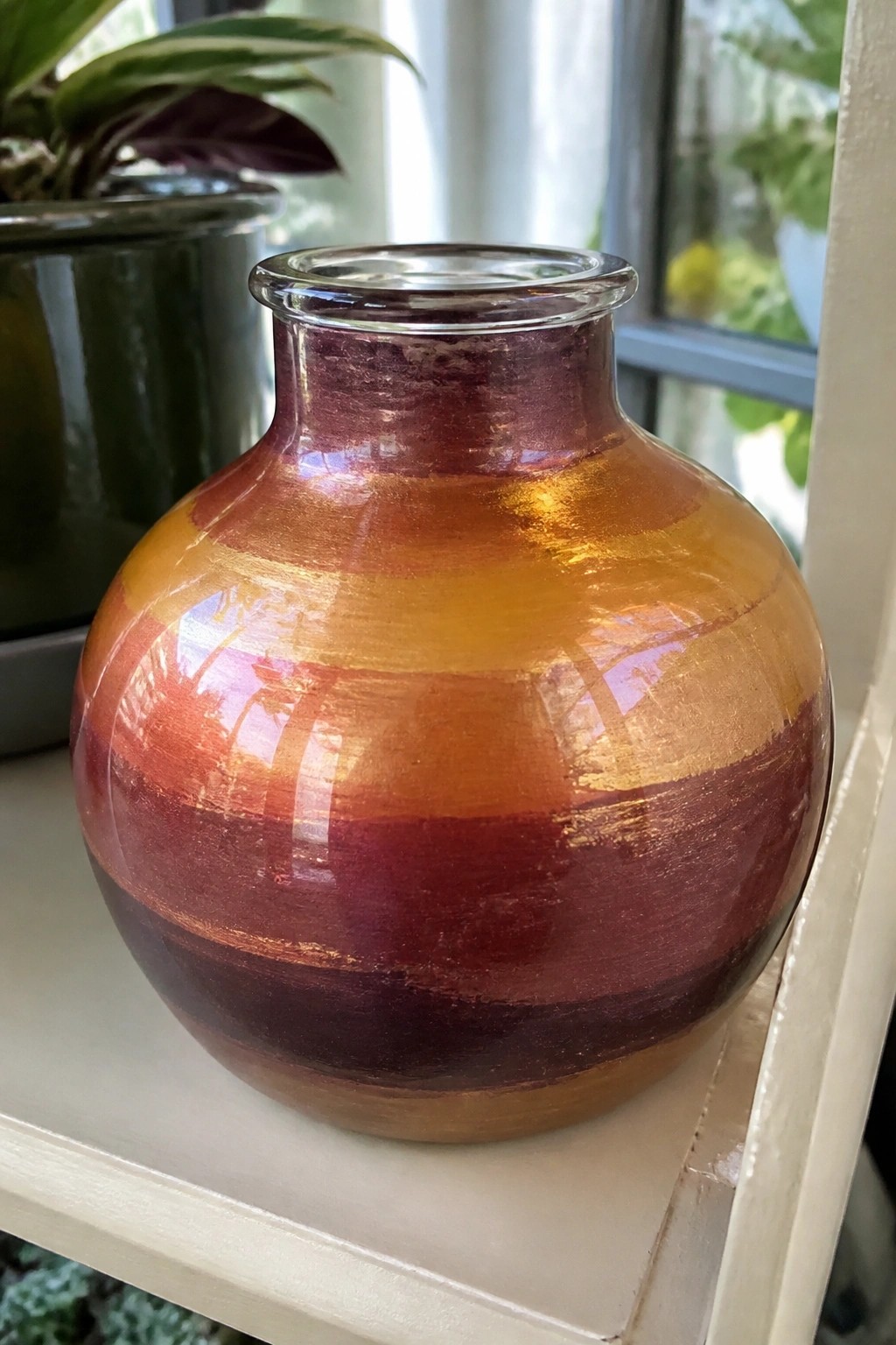 Round glass vase with horizontal red orange and yellow stripes on shelf