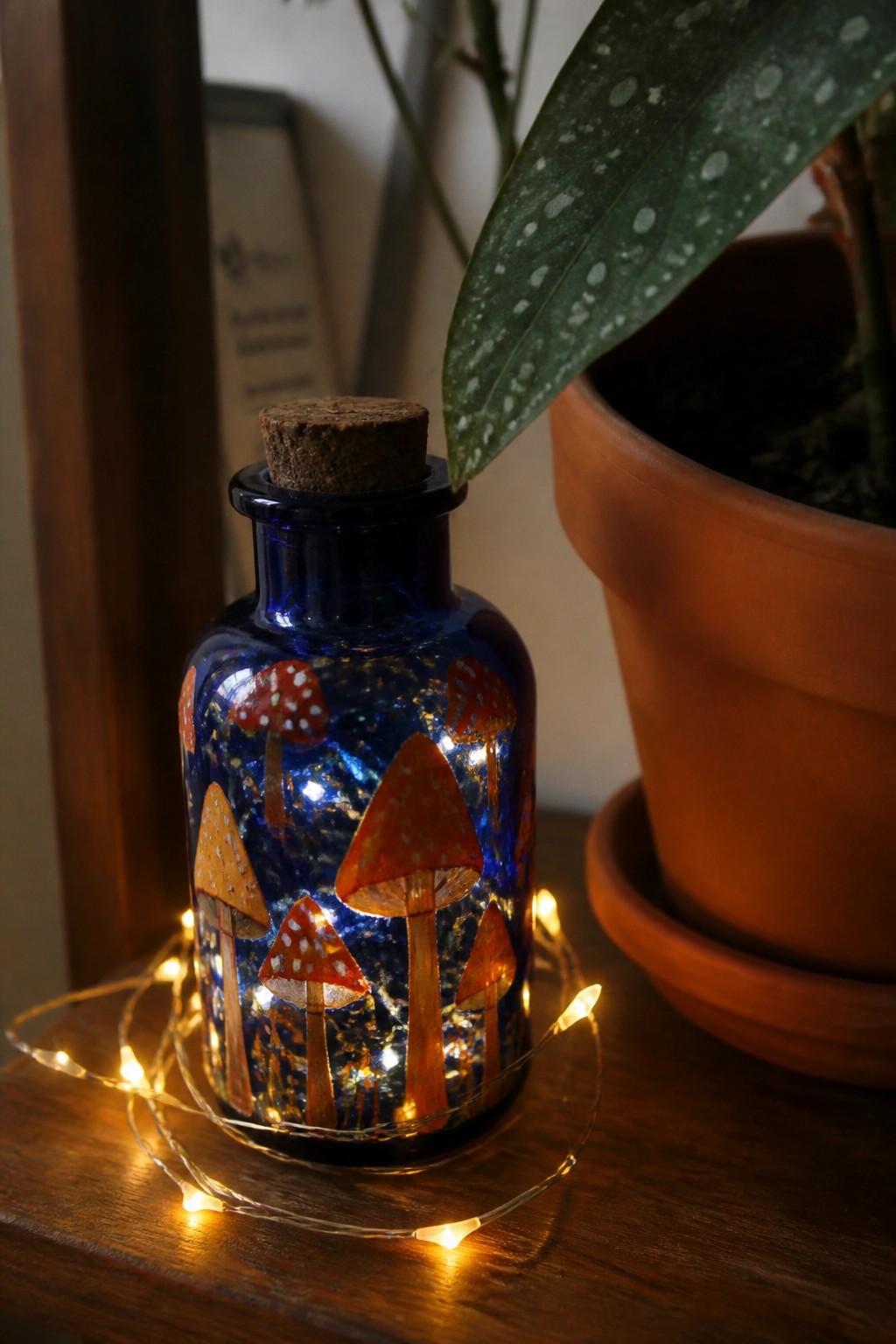 Blue glass bottle with mushroom designs wrapped in glowing string lights on wood