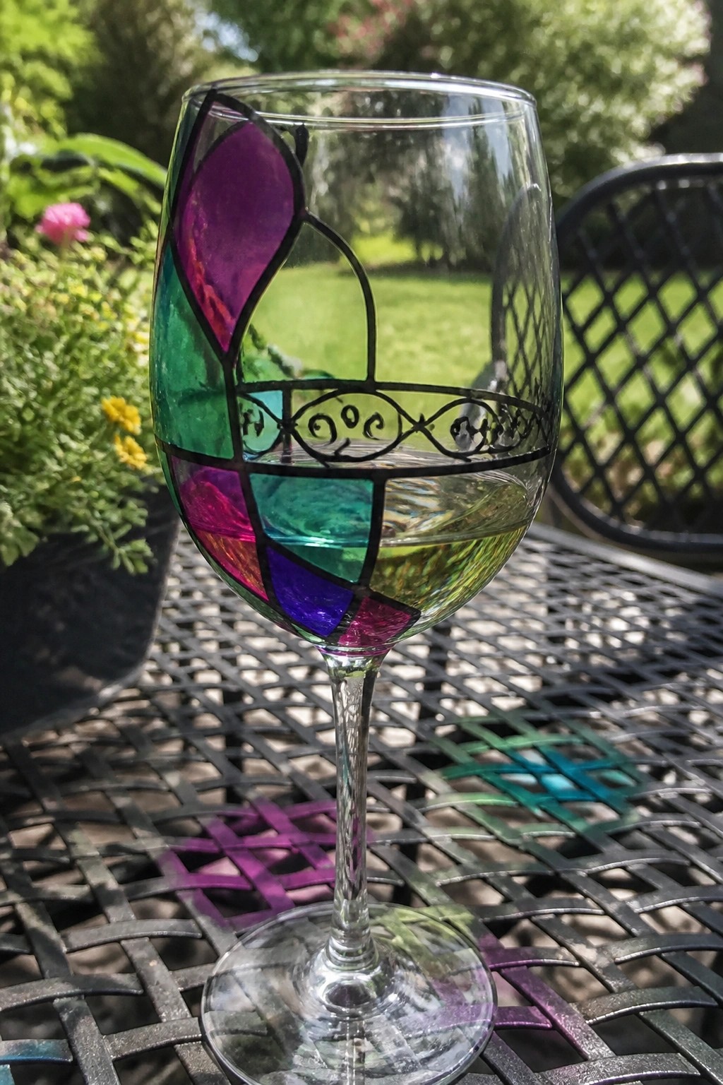 Colorful stained-glass wine glass with liquid on black metal garden table
