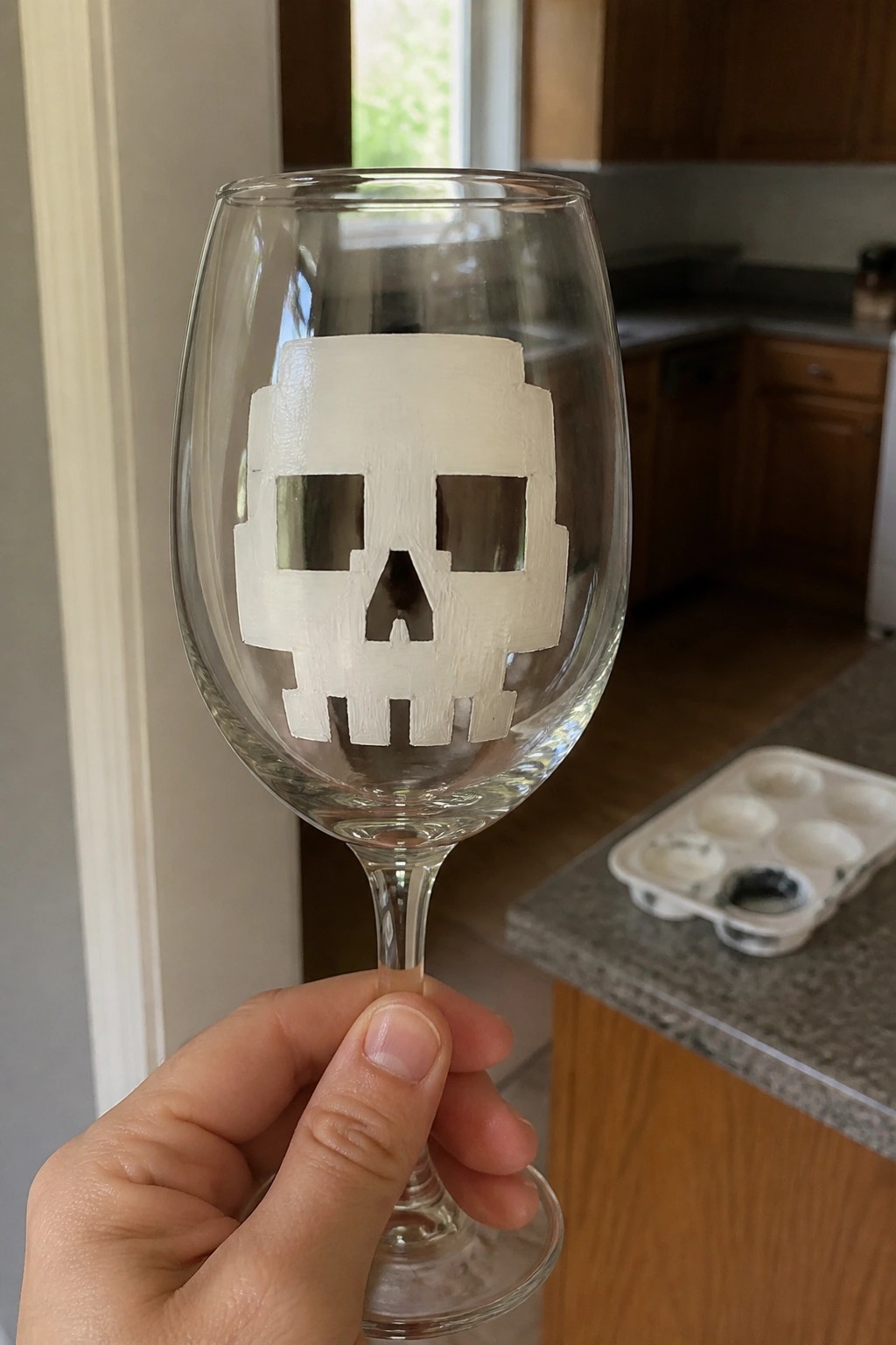 Hand holding wine glass etched with white pixelated skull design in kitchen