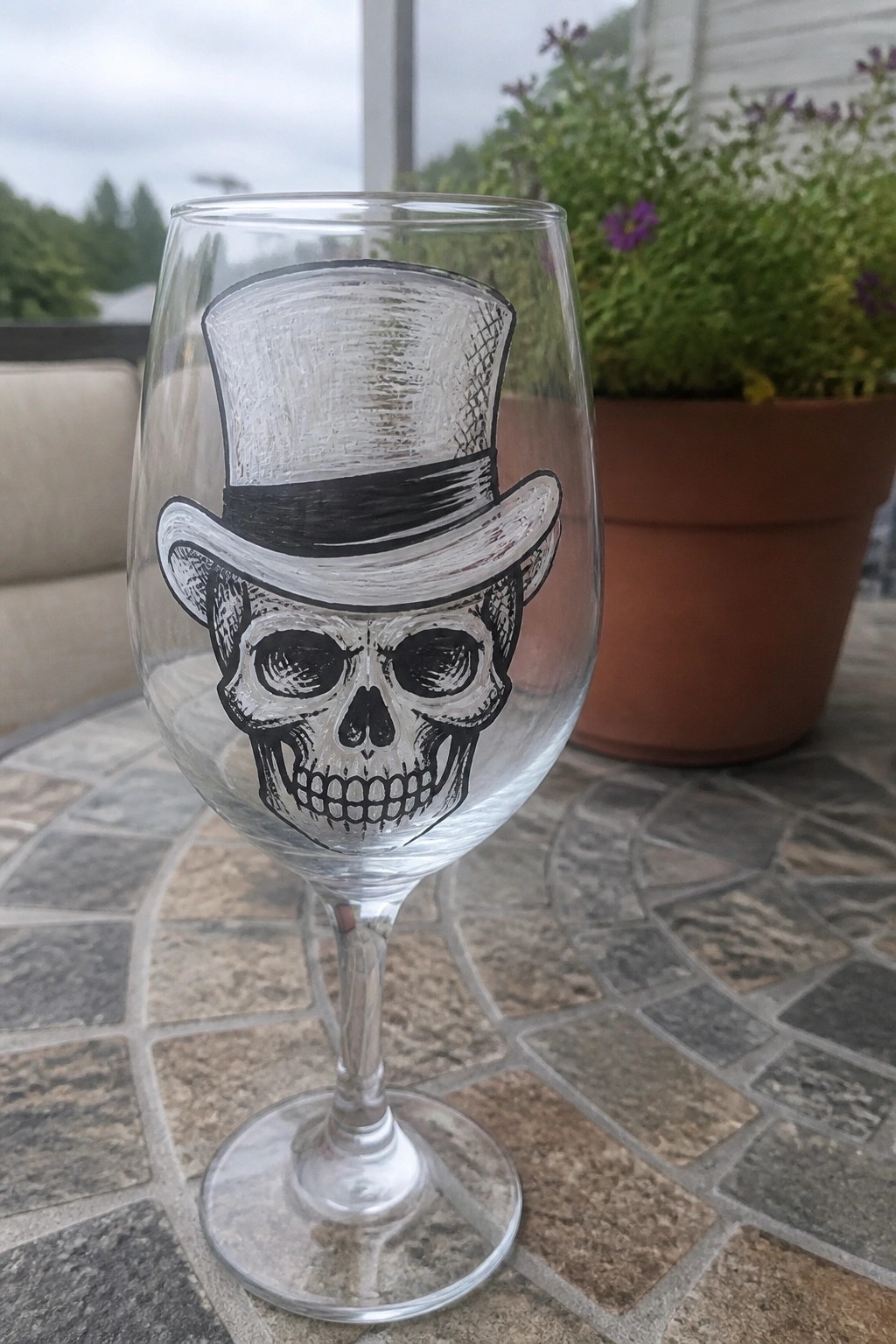 Wine glass painted with skull wearing top hat on stone outdoor table