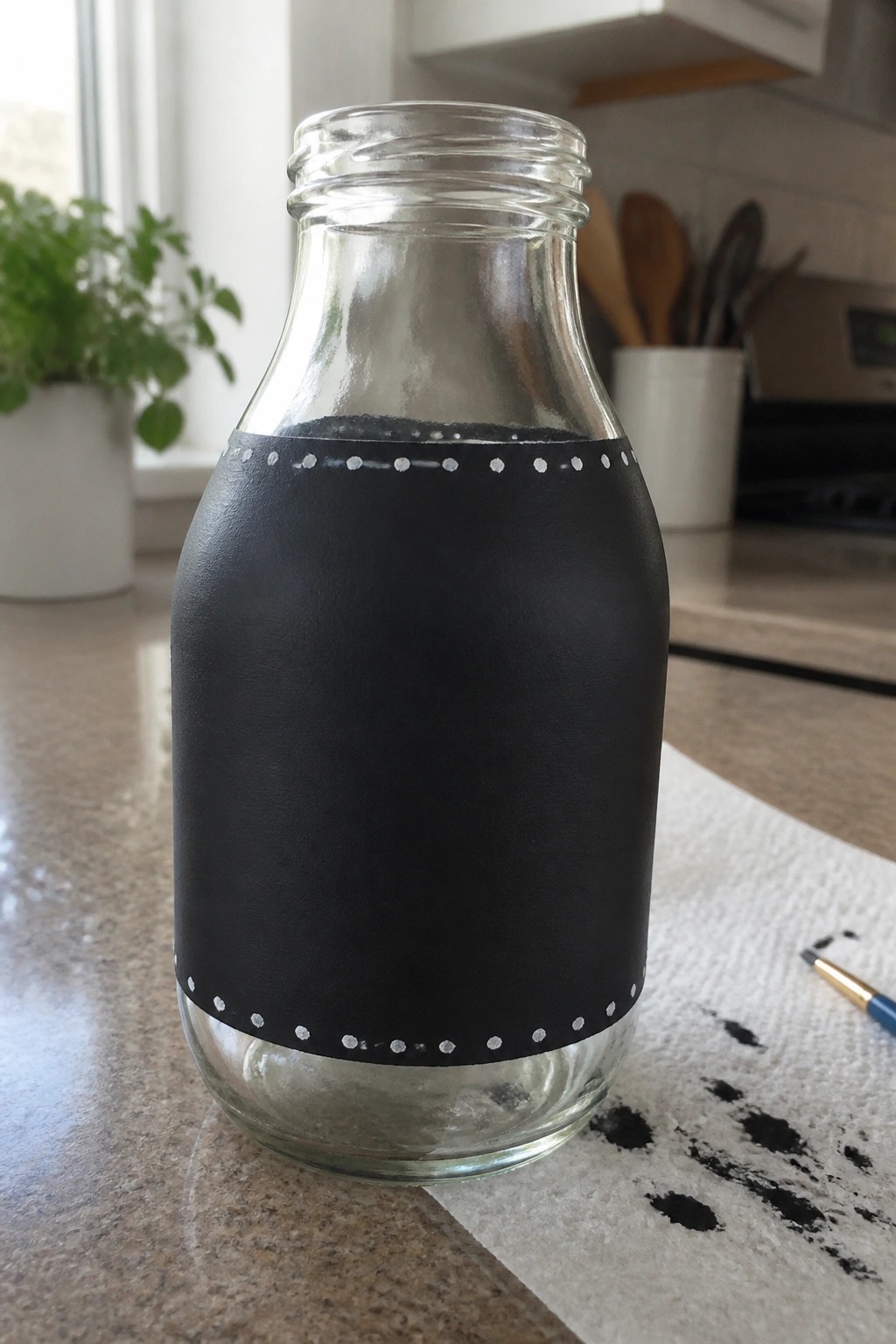 Clear glass bottle with black chalkboard band and white dotted borders on counter