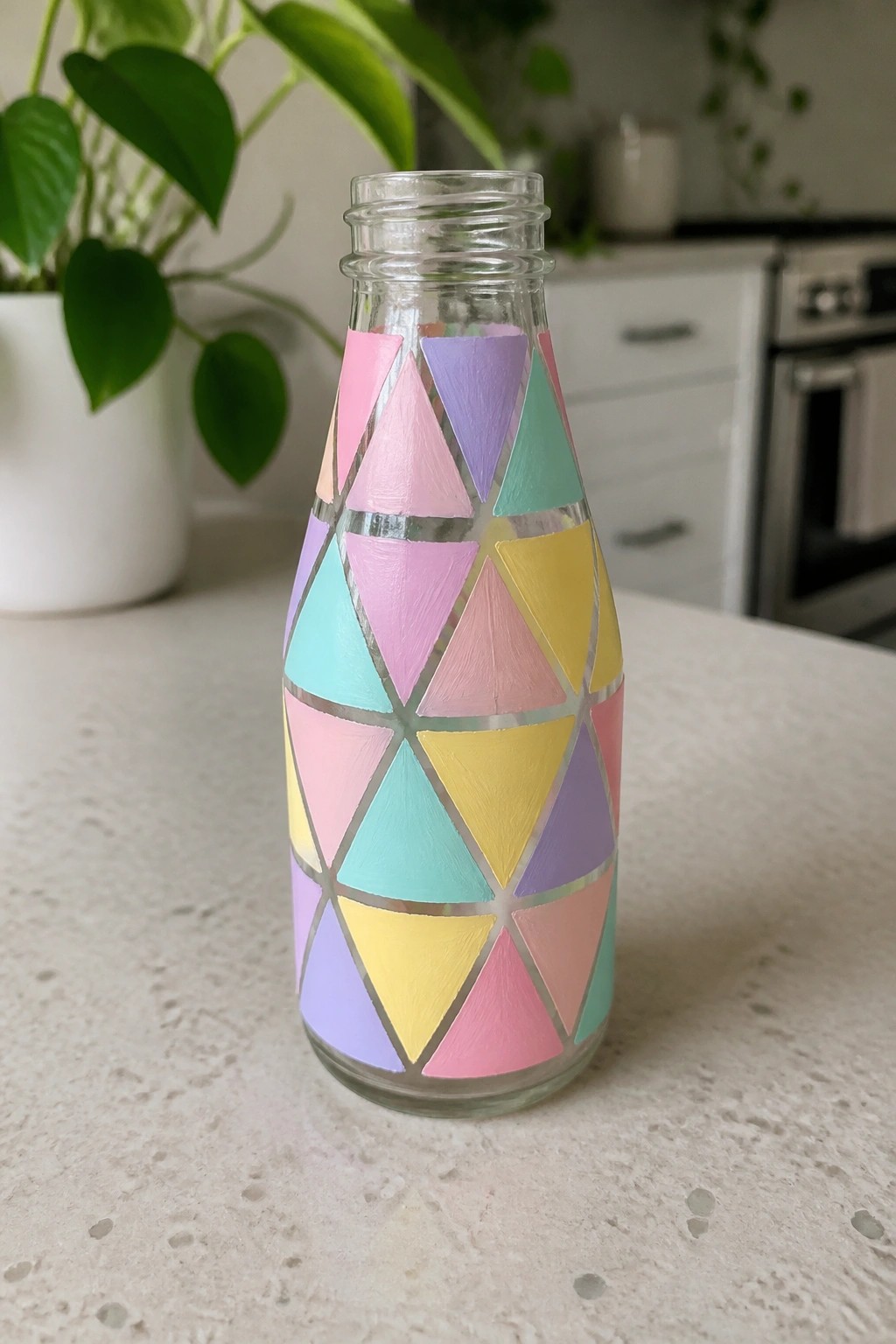 Glass bottle decorated with pastel triangles and silver geometric lines on countertop