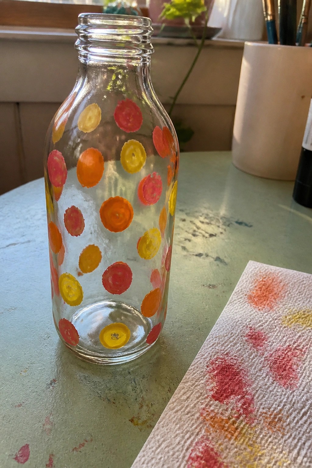 Clear glass bottle with red, orange, and yellow painted dots on green table