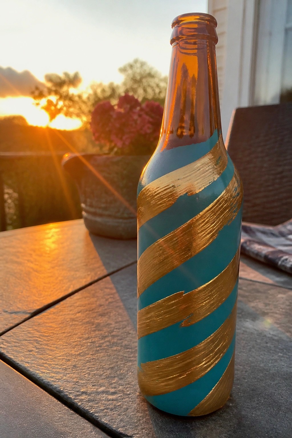 Teal and gold striped glass bottle on wooden table at sunset