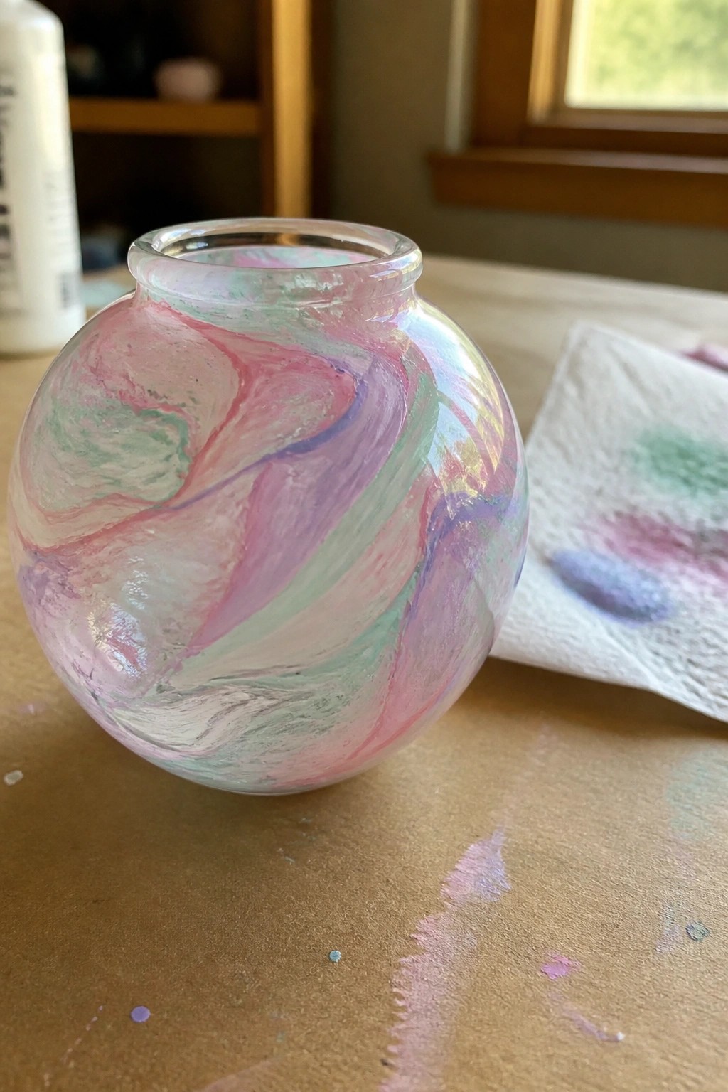 Round glass vase swirled with pink, purple, and mint green paint on wooden table