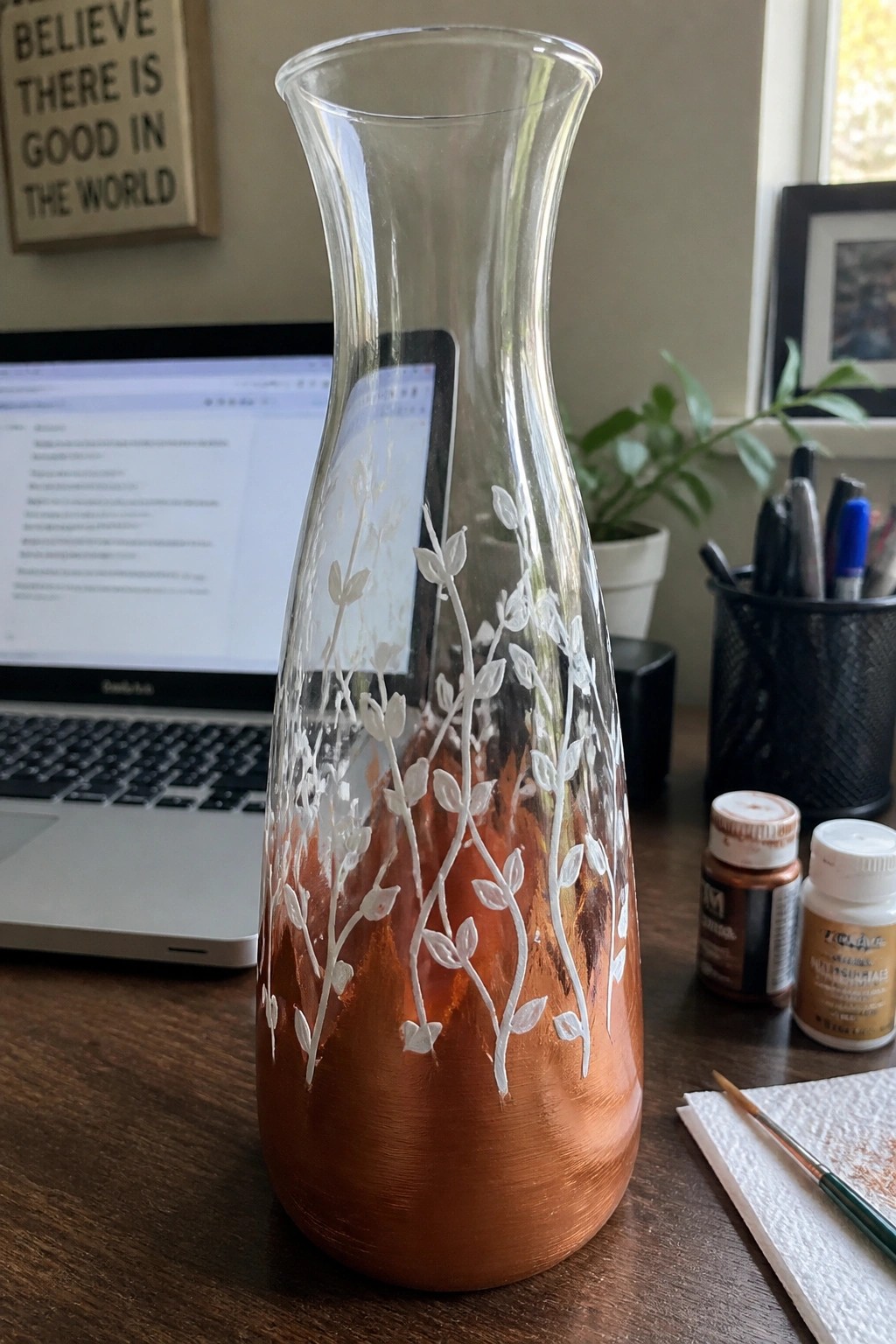 Glass vase with copper-orange base and white leafy vine designs on desk