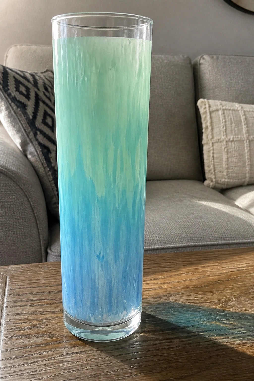 Tall clear glass with blue-to-green streaked paint on wooden table