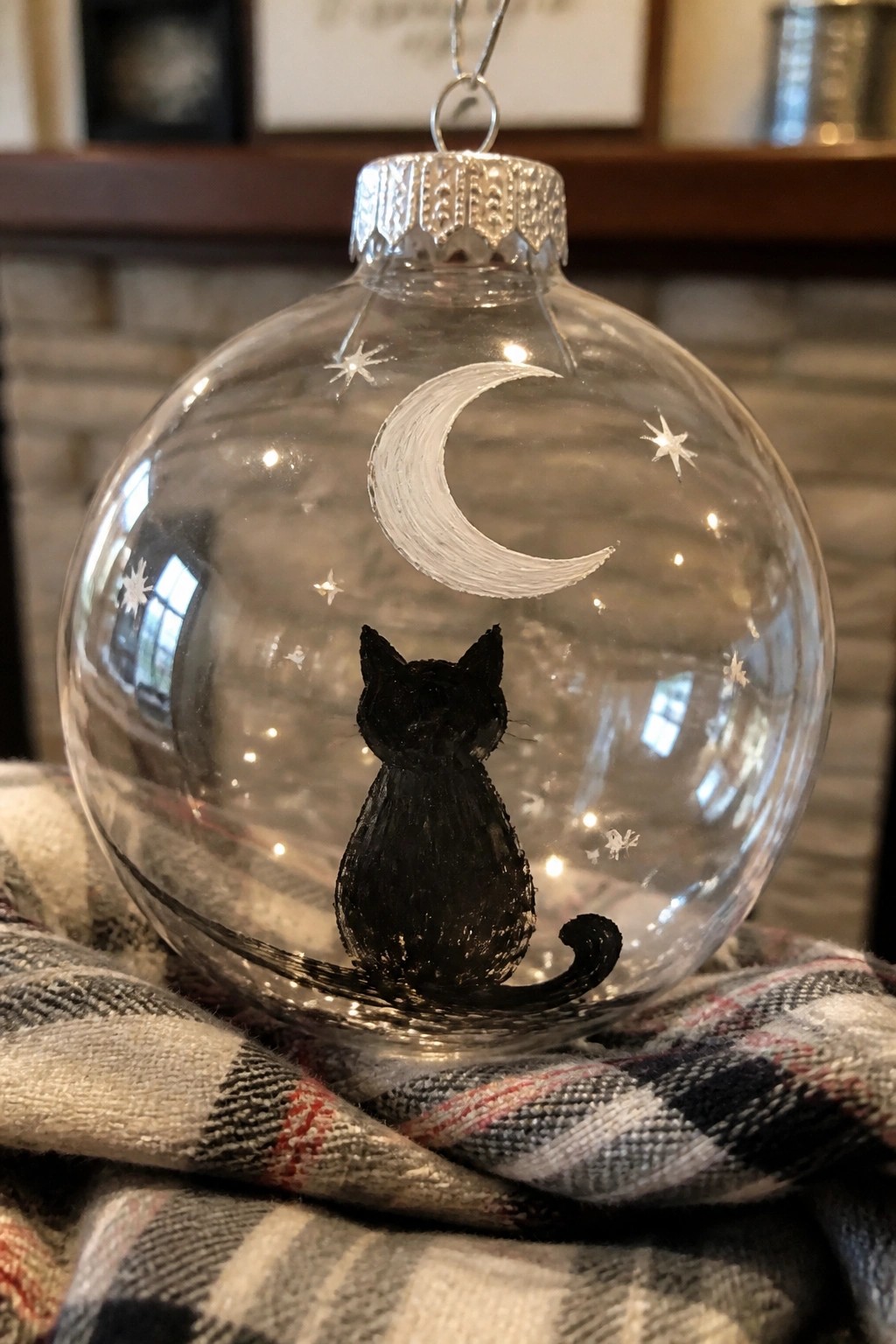 Transparent glass ornament with black cat, white crescent moon and stars on plaid fabric.