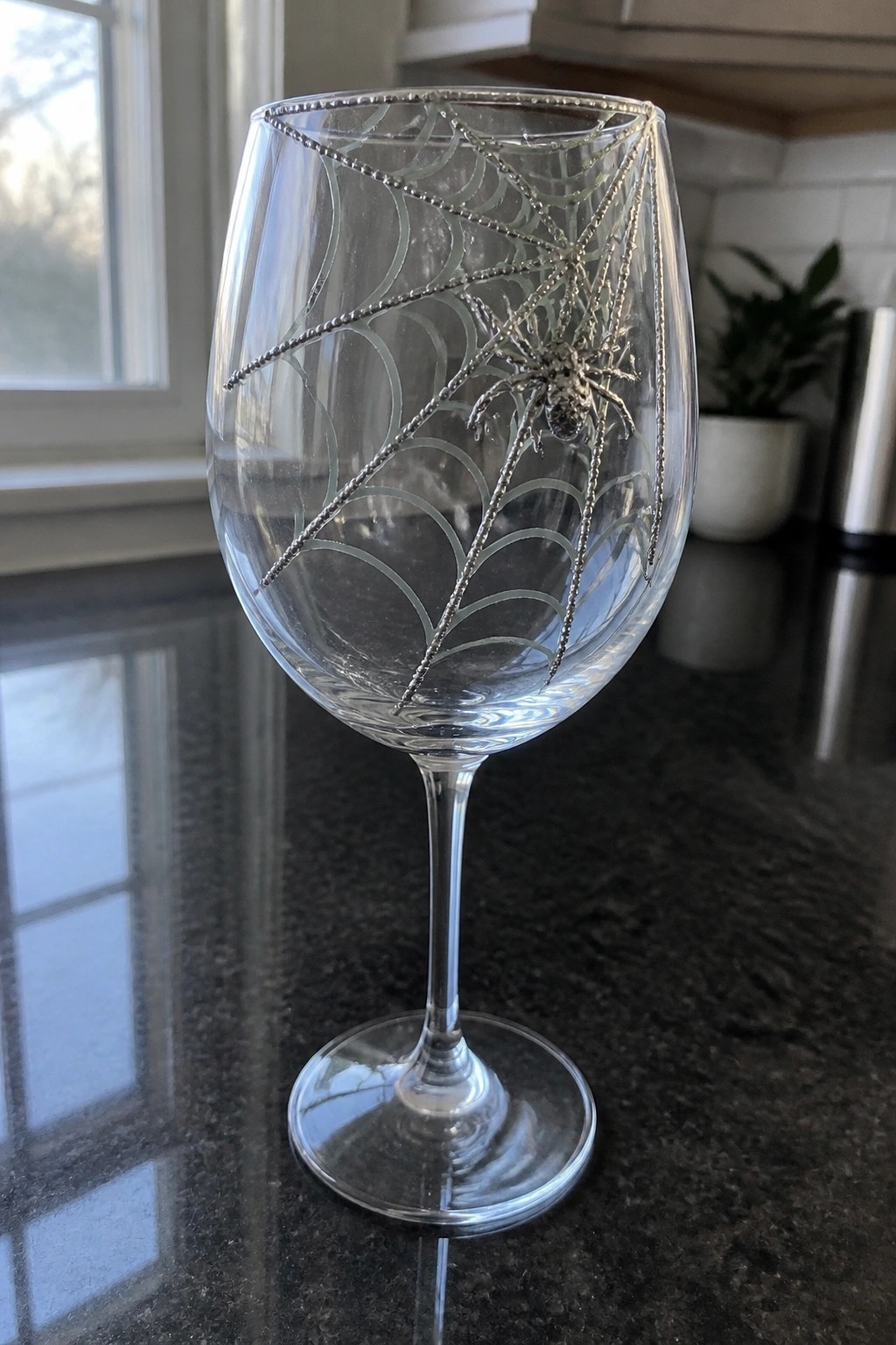 Clear wine glass with silver spiderweb and spider on dark countertop