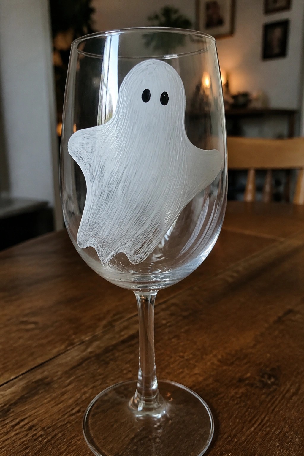 Clear wine glass with white ghost and black eyes on wooden table.