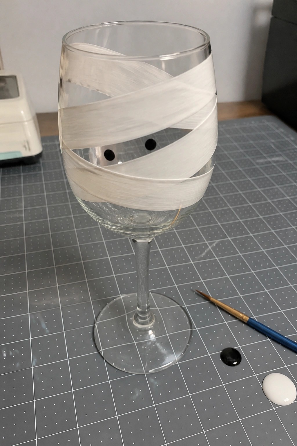 Wine glass with spiraling white paint bands and black eyes on gray mat