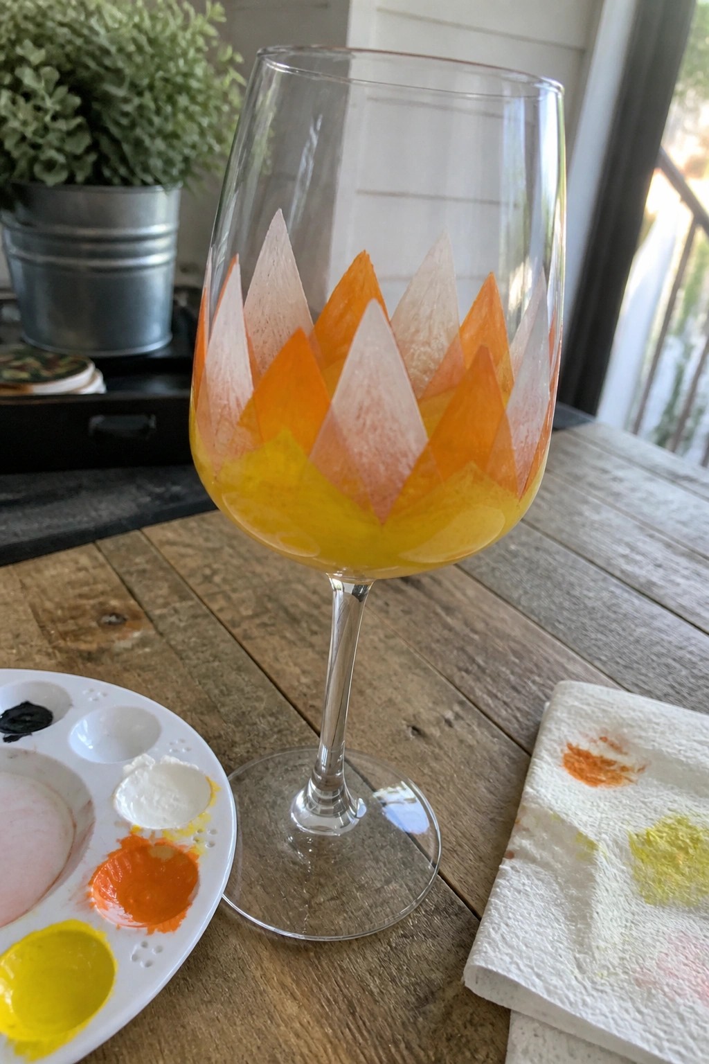 Wine glass with orange-yellow triangular paint pattern beside palette on wooden table
