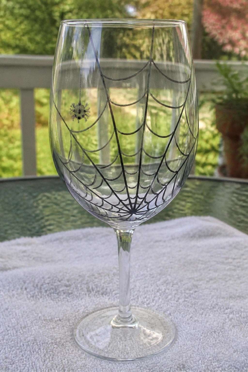 Clear wine glass with black spiderweb design and spider on white cloth outdoors.
