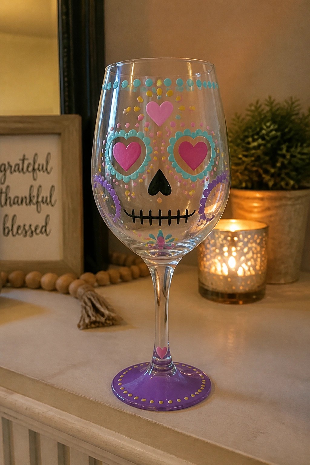 Painted wine glass with colorful sugar skull design, pink hearts, and purple base.