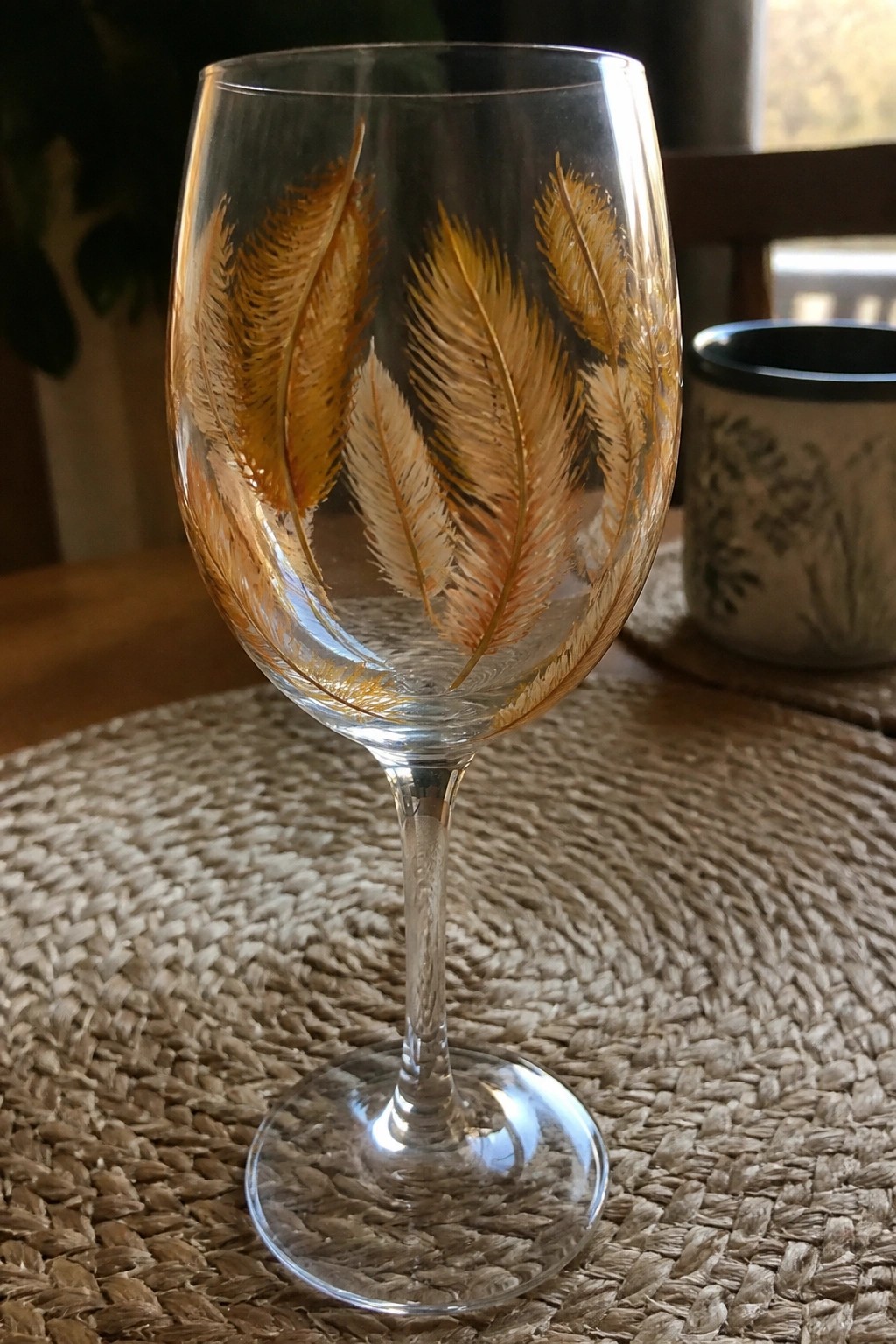 Stemmed wine glass with golden feather designs on woven placemat