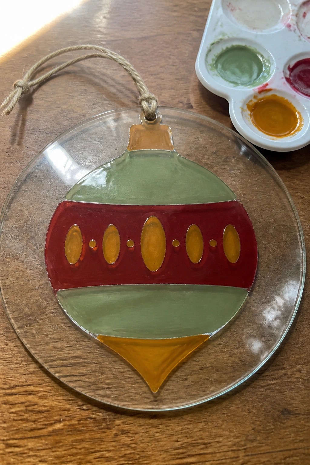 Stained glass Christmas ornament with red, green, and yellow sections beside paint palette