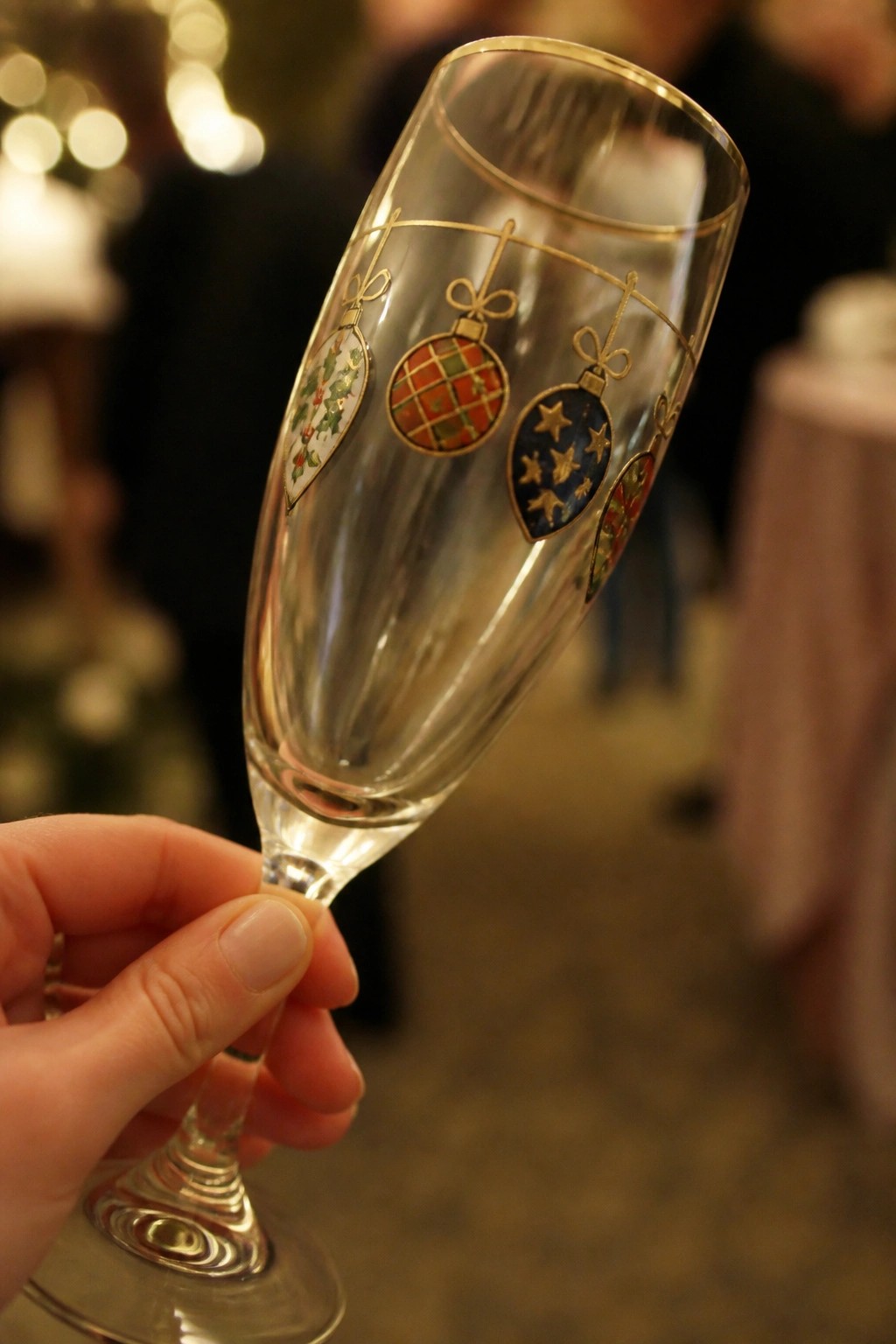 Hand holding a gold-trimmed champagne flute decorated with colorful Christmas ornaments.
