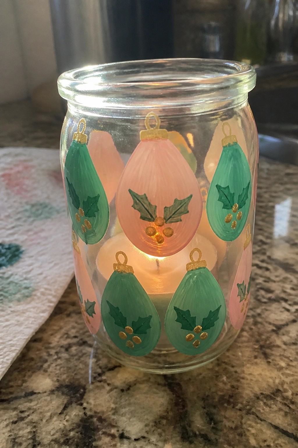 Glass jar hand-painted with pink and green Christmas ornaments containing a lit candle