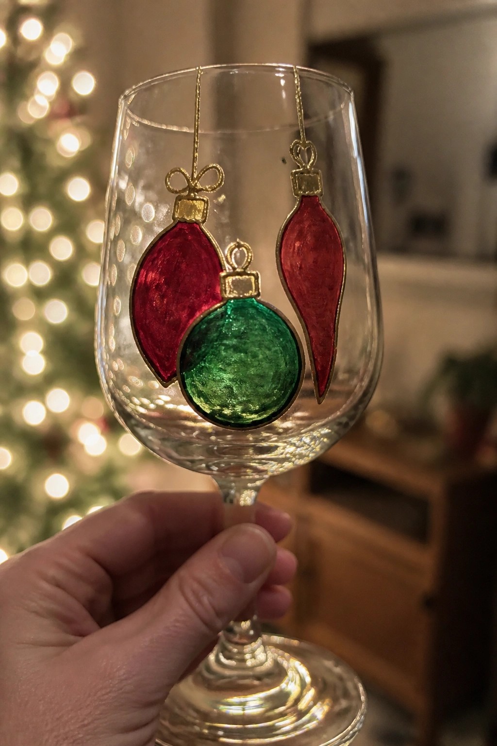 Hand holding wine glass with red and green stained-glass Christmas ornaments