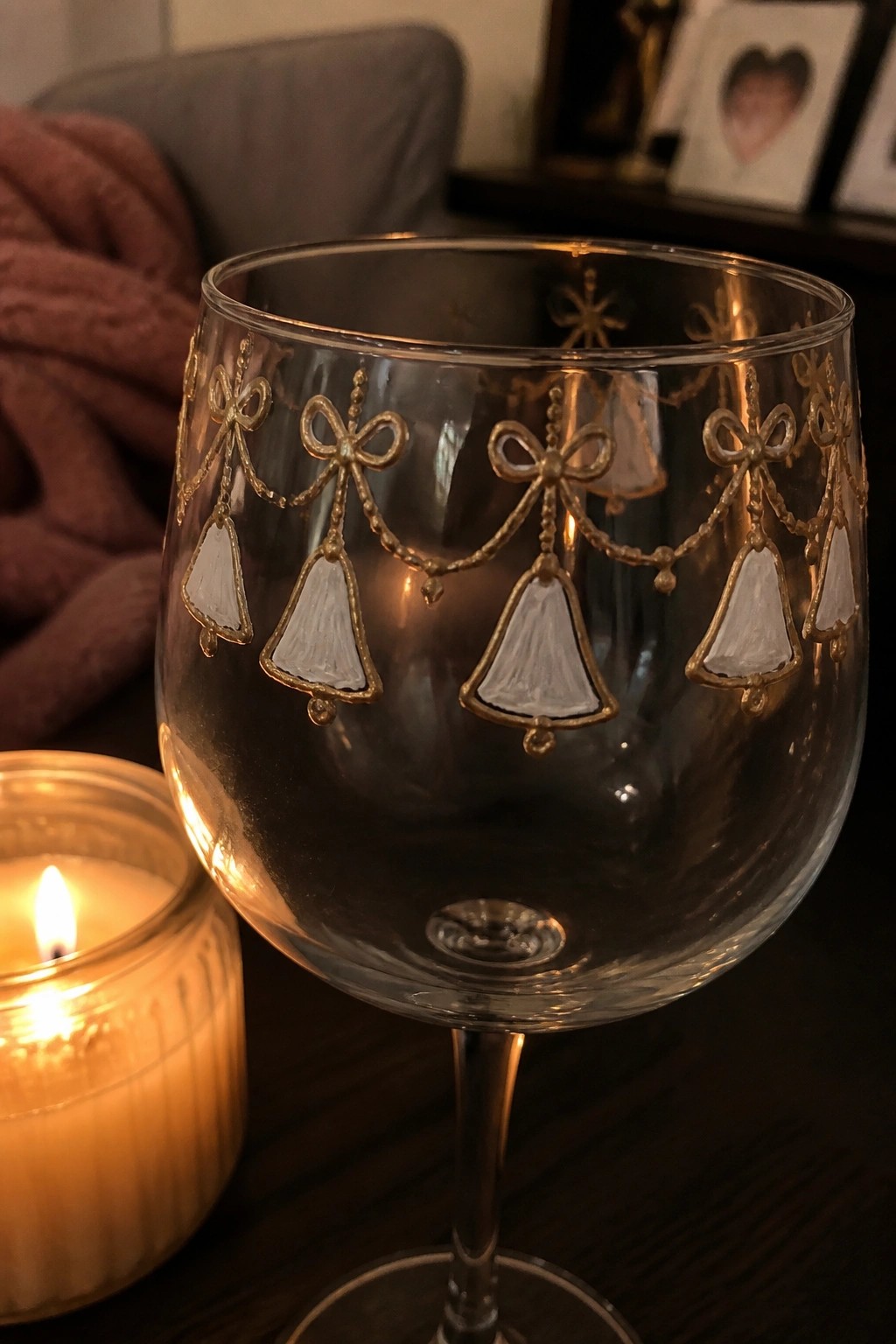 Decorative wine glass with gold bows and bells beside lit candle on wood table