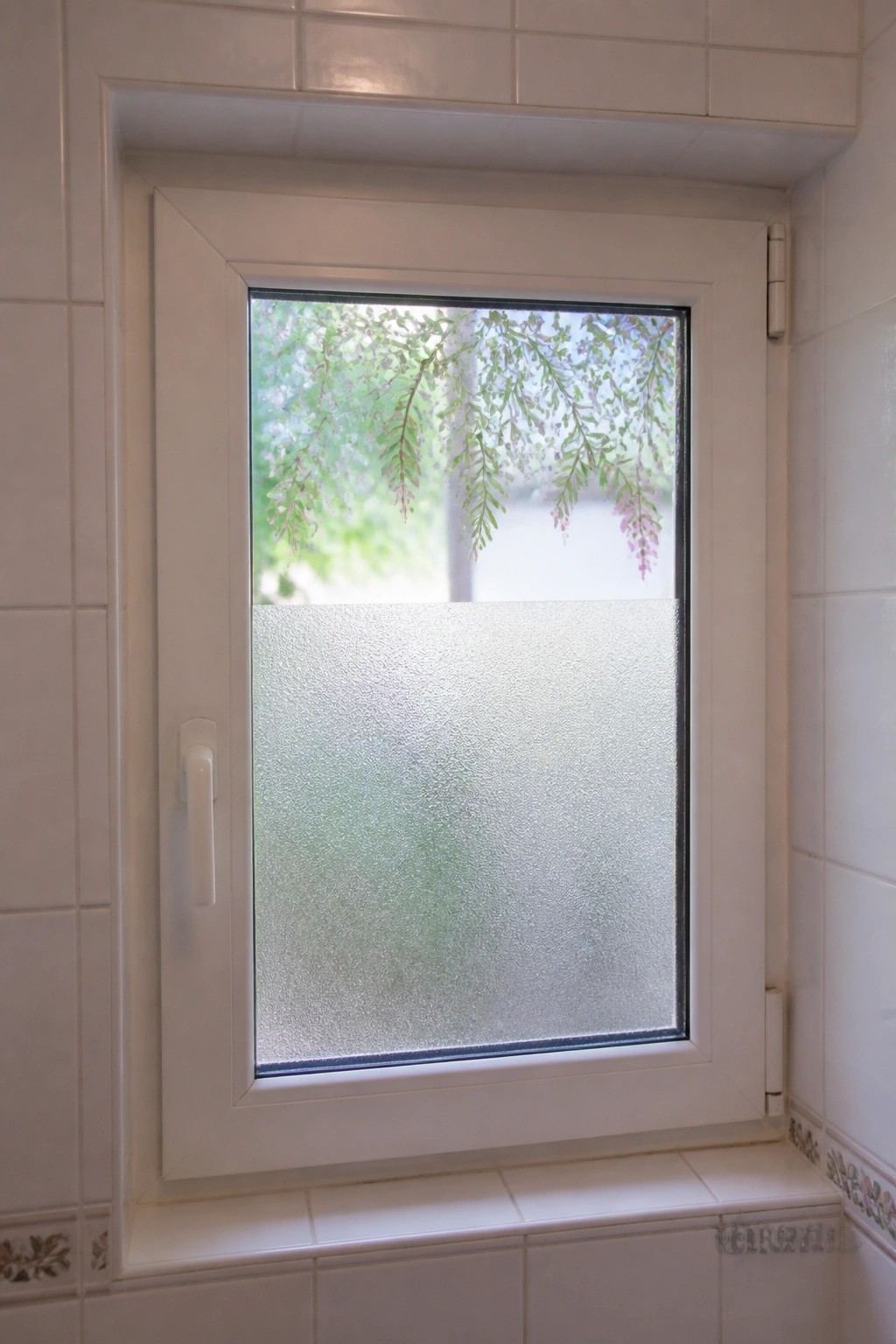 White casement window with frosted lower half and green foliage visible above.