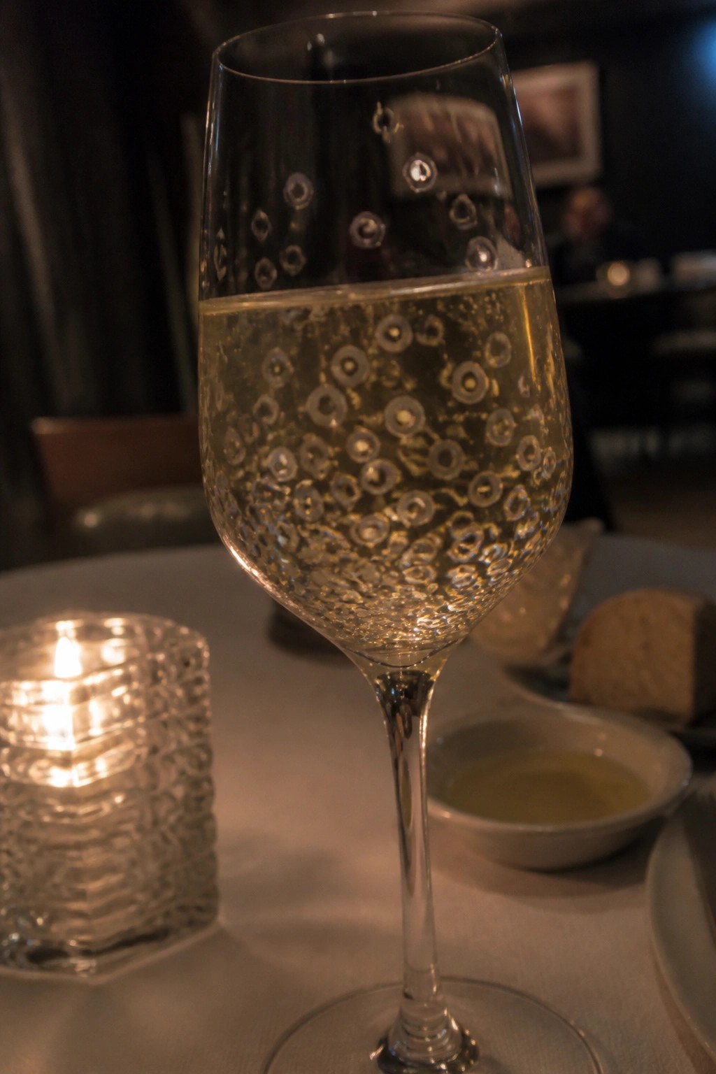 Sparkling wine in a patterned glass beside a lit candle on a table