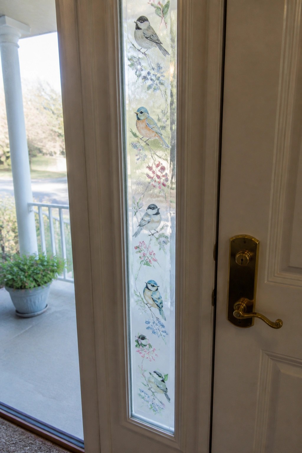 White door with vertical glass panel painted with chickadees and gold handle