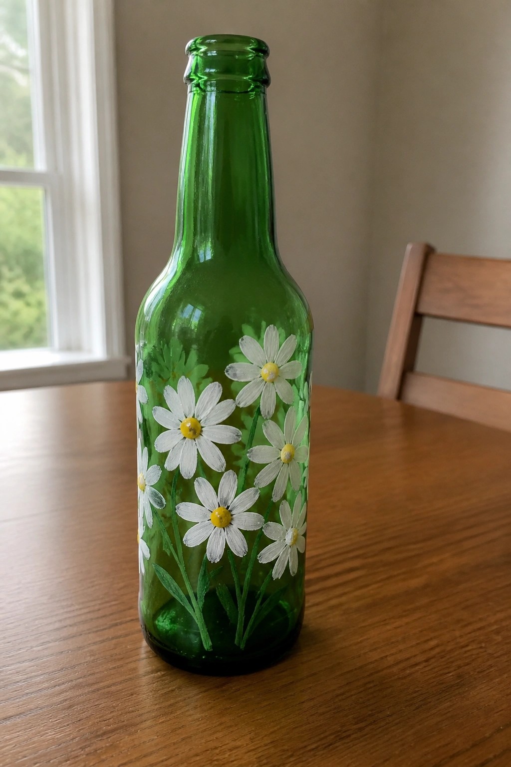 Green glass bottle hand-painted with white daisies and leaves on wooden table.