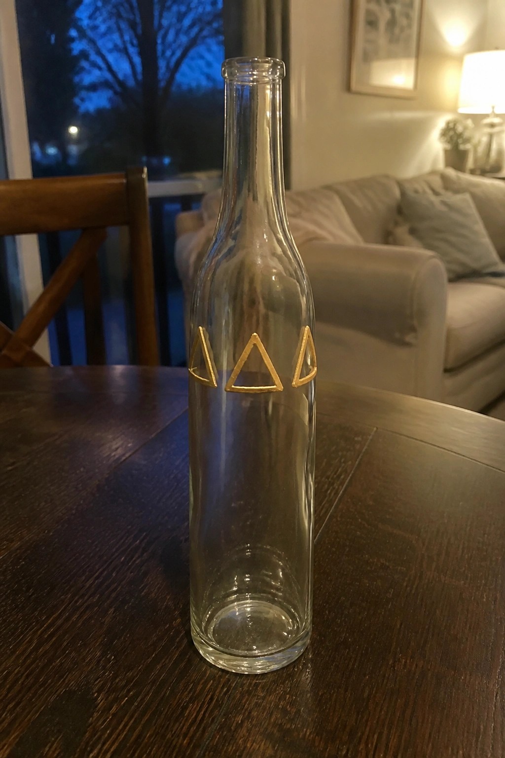 Empty glass bottle with three gold triangle symbols on dark wooden table in living room