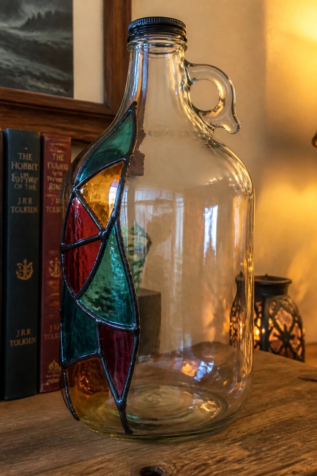 Handled glass jug with vibrant stained glass leaf beside Tolkien books