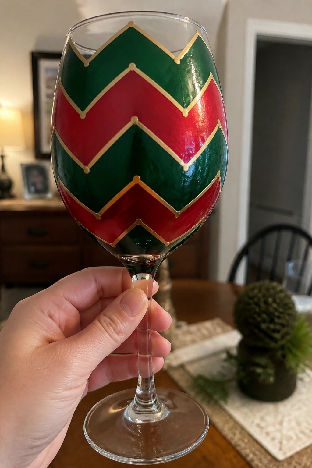 Hand holding wine glass with red and green chevron patterns and gold trim.