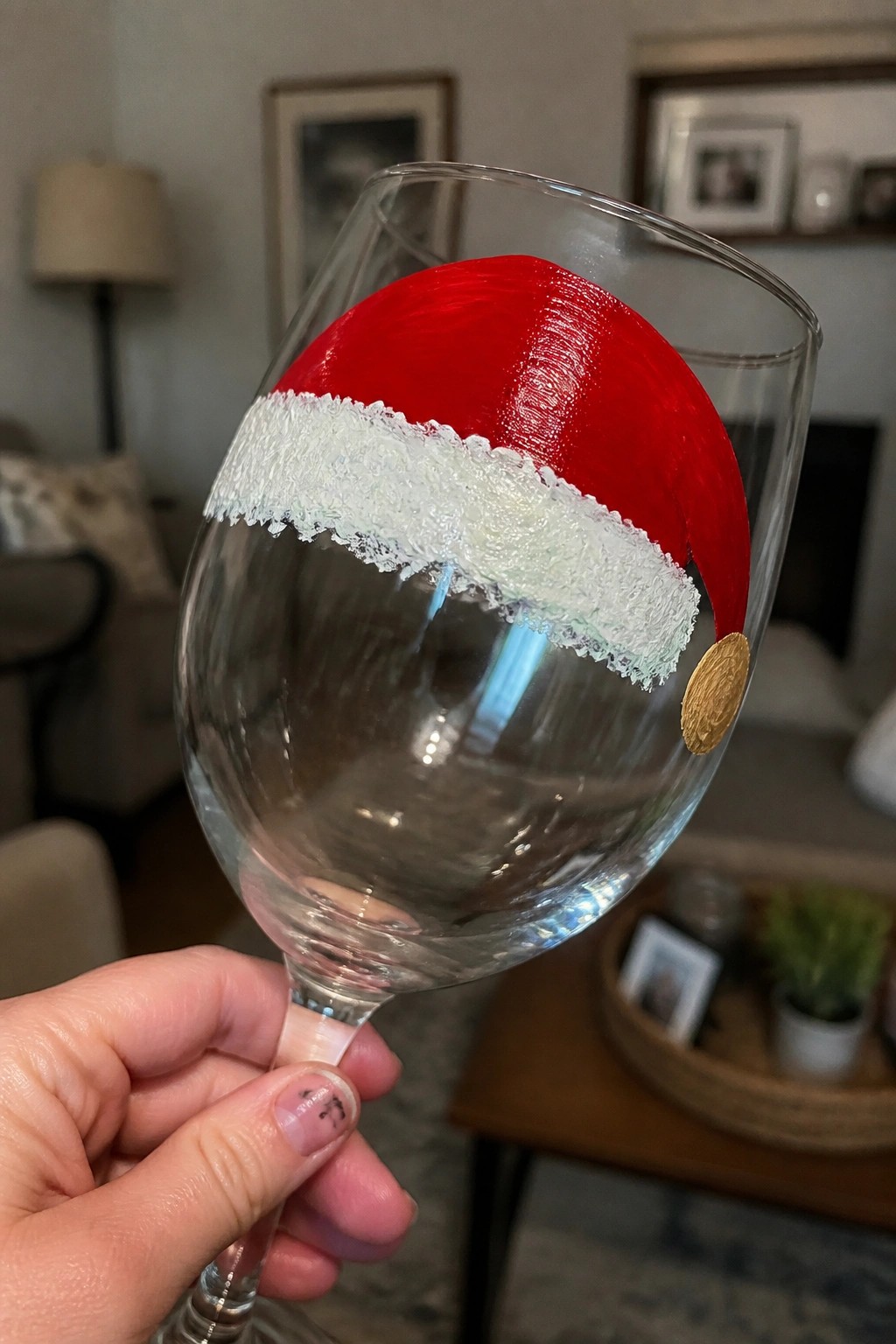 Hand holding wine glass painted with red Santa hat, white brim, and gold pom-pom