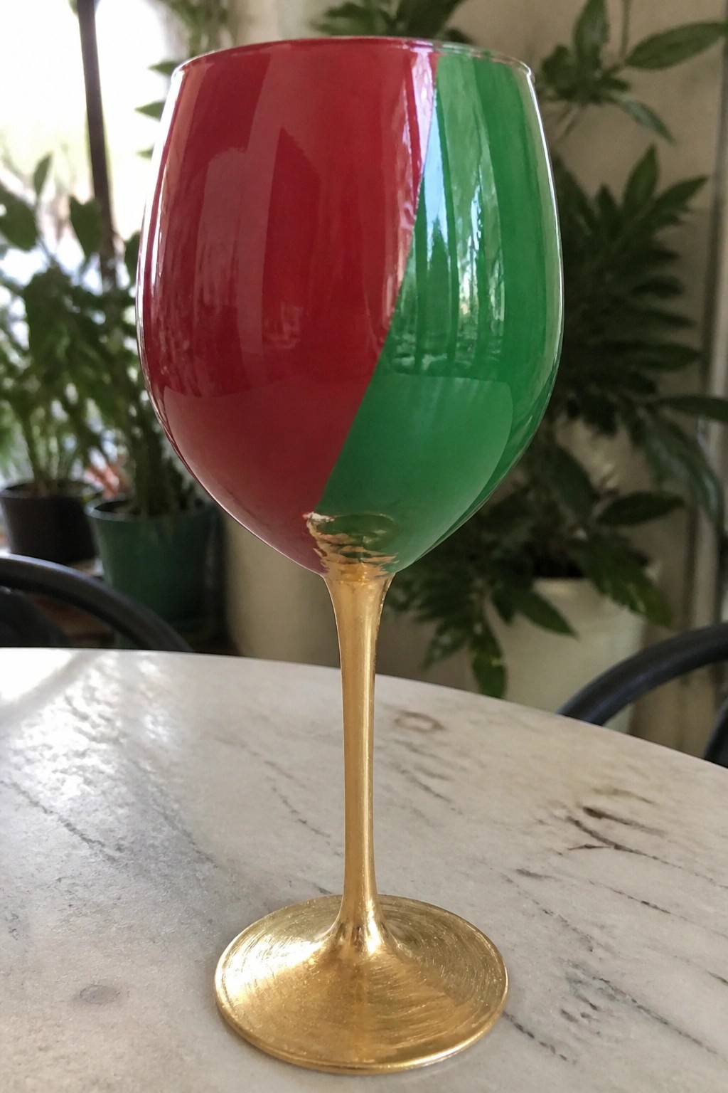 Red and green painted wine glass with gold stem on marble table