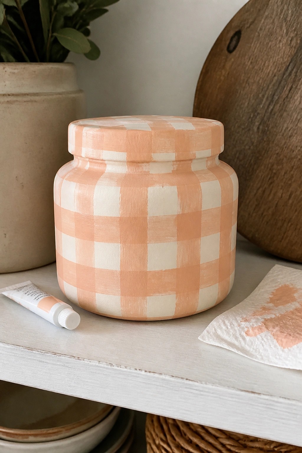Peach and white gingham-painted jar on white shelf with paint tube